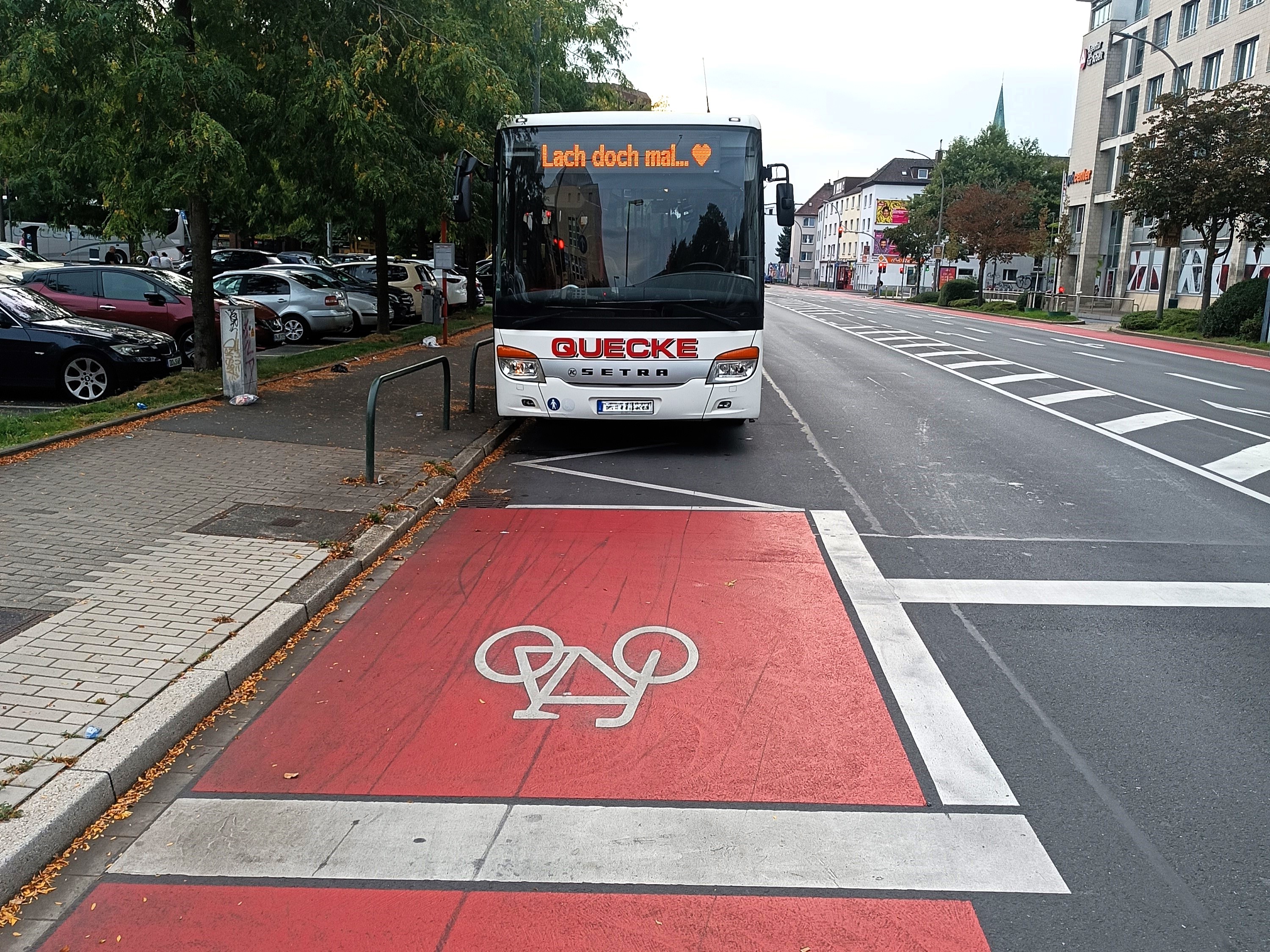 Ein Bus pausiert an einer Bushaltestelle. Auf der selben Spur verläuft ein Radfahrstreifen. Die rote Farbe beginnt dort, wo der Bus endet. 