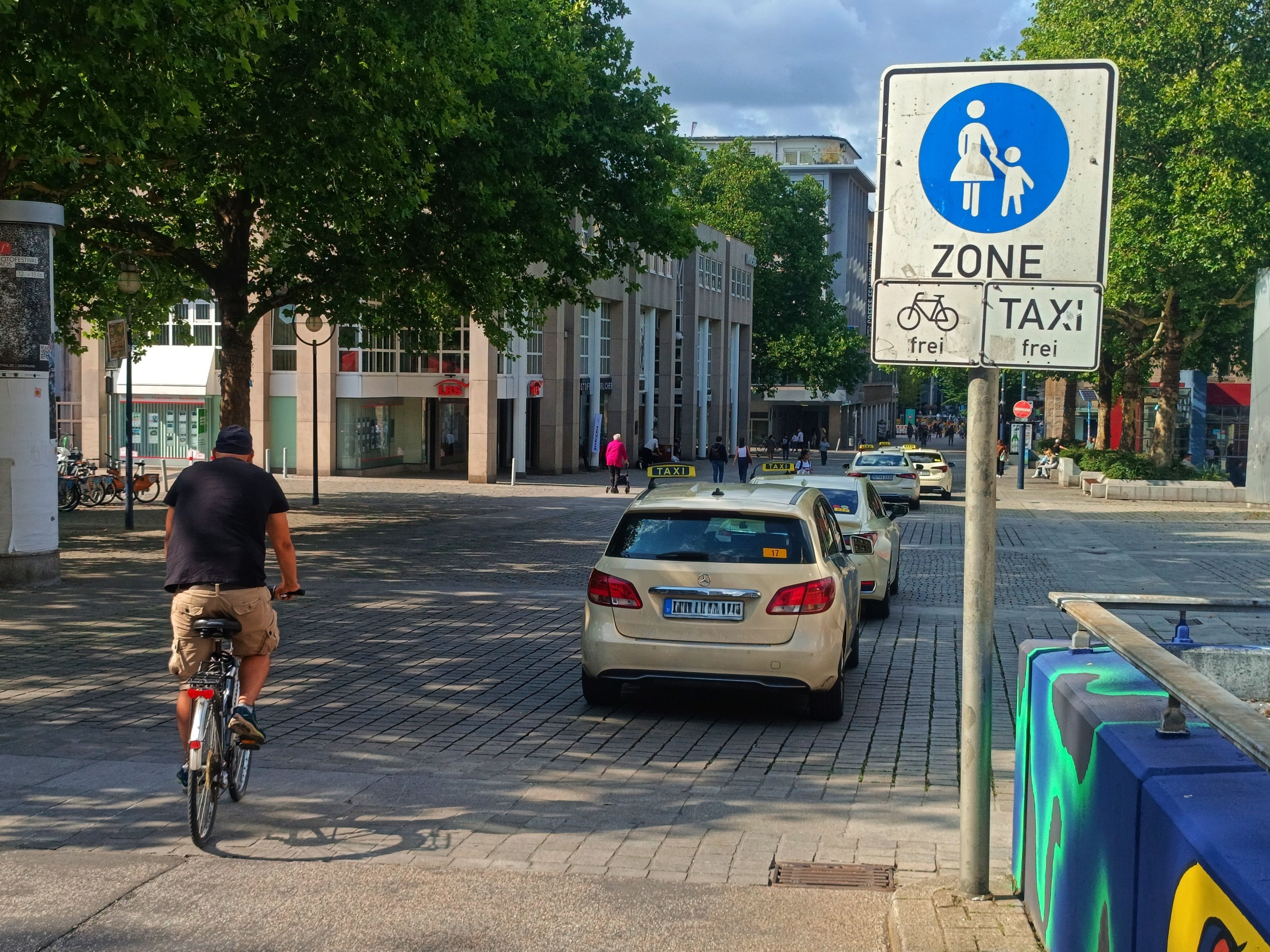 Links ein Radfahrender von hinten. Rechts das Schild für eine Fußgängerzone mit der Freigabe von Radverkehr und Taxis. 