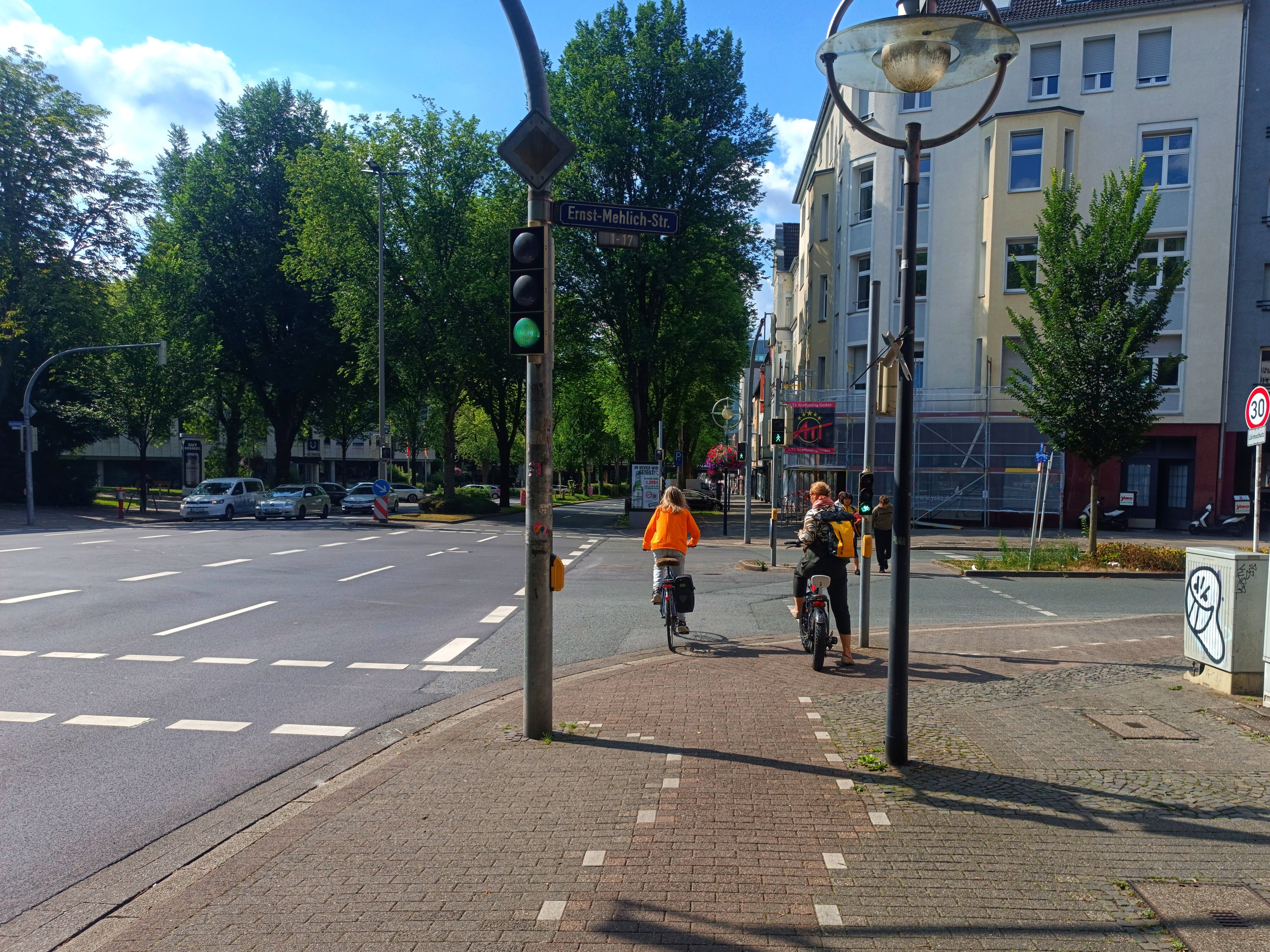 Radweg an der Kreuzung von Märkische Straße und Ernst-Melich-Straße. Zwei Radfahrende überqueren die Kreuzung. 