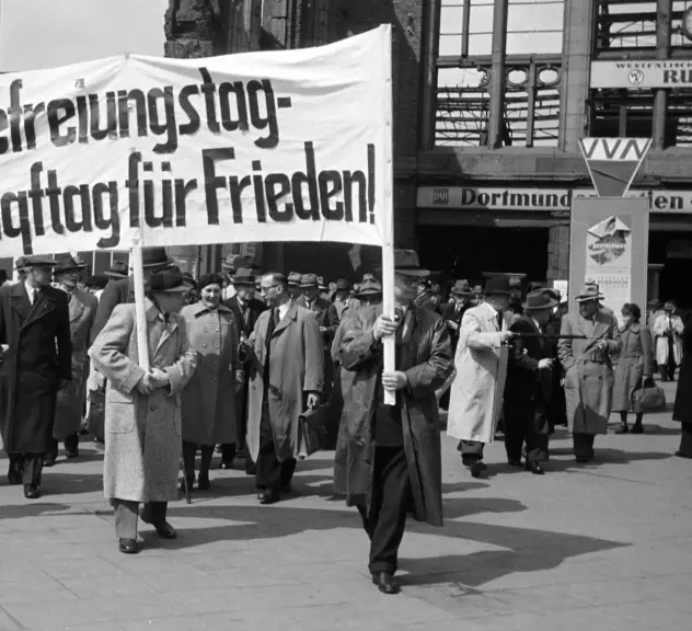 Eine Menschenmenge bei einer Kundgebung, die ein Banner mit der Aufschrift Befreiungstag, Kampftag für Frieden tragen.