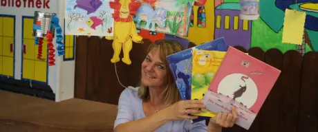 Eine Frau hält drei Kinderbücher in ihren Händen und hält sie hoch 