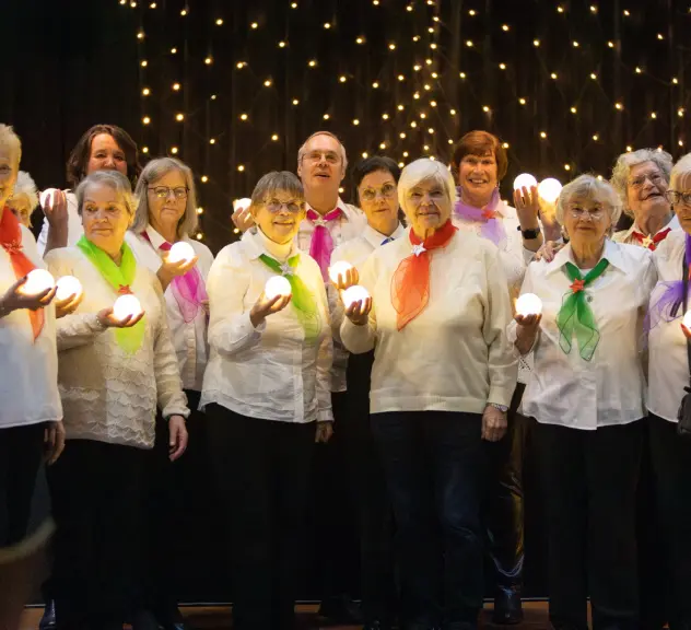 Ein Foto des Chors in weißer Kleidung, bunten Tüchern und Lichtern bekleidet