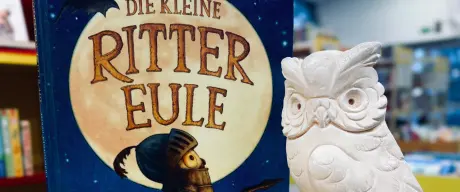 Das Buch "Die kleine Rittereule" steht auf einem Tisch neben einer weißen Figur einer Eule