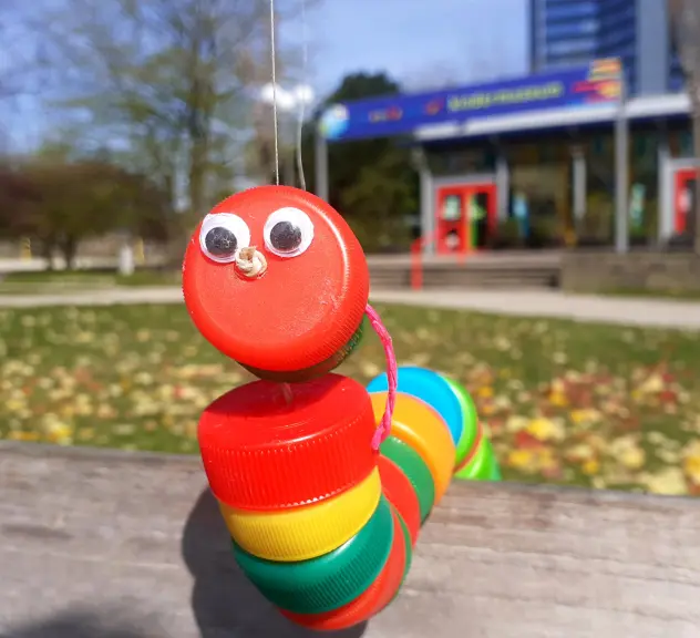 Eine bunte Wurmmarionette aus Deckeln von Plastikflaschen mit aufgeklebten Augen 