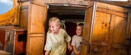 Zwei kleine Kinder gehen durch eine Holztür, die zu einem Boot gehört.