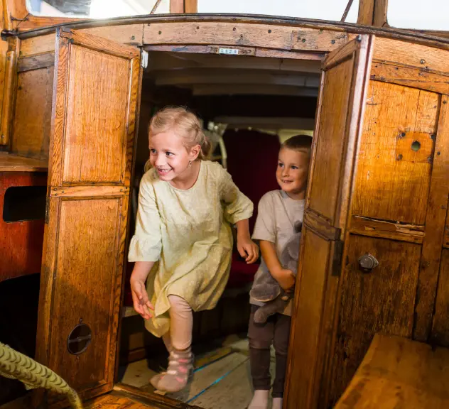 Zwei kleine Kinder gehen durch eine Holztür, die zu einem Boot gehört.